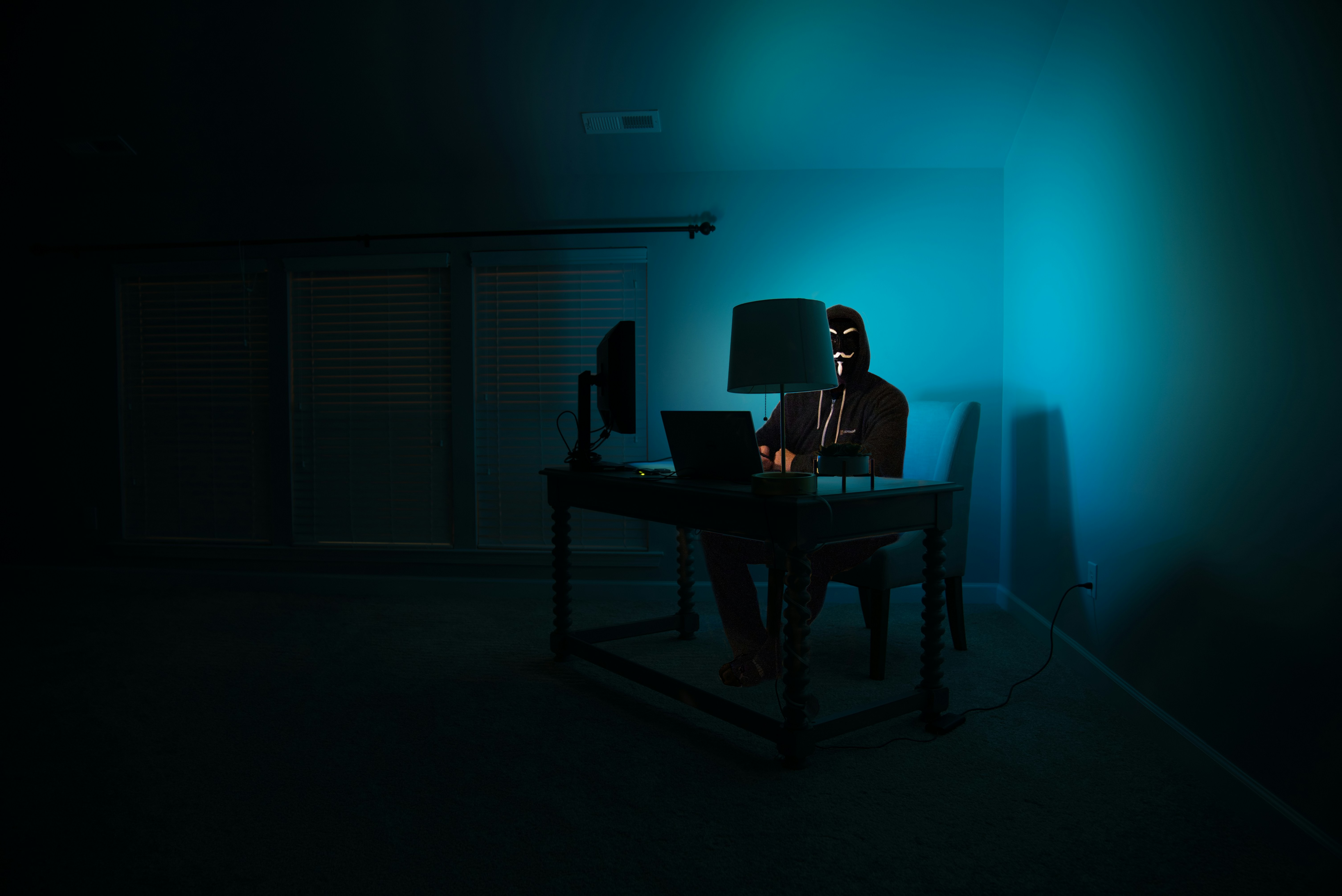 Desk with a person wearing a mask working on a computer in dim lighting
